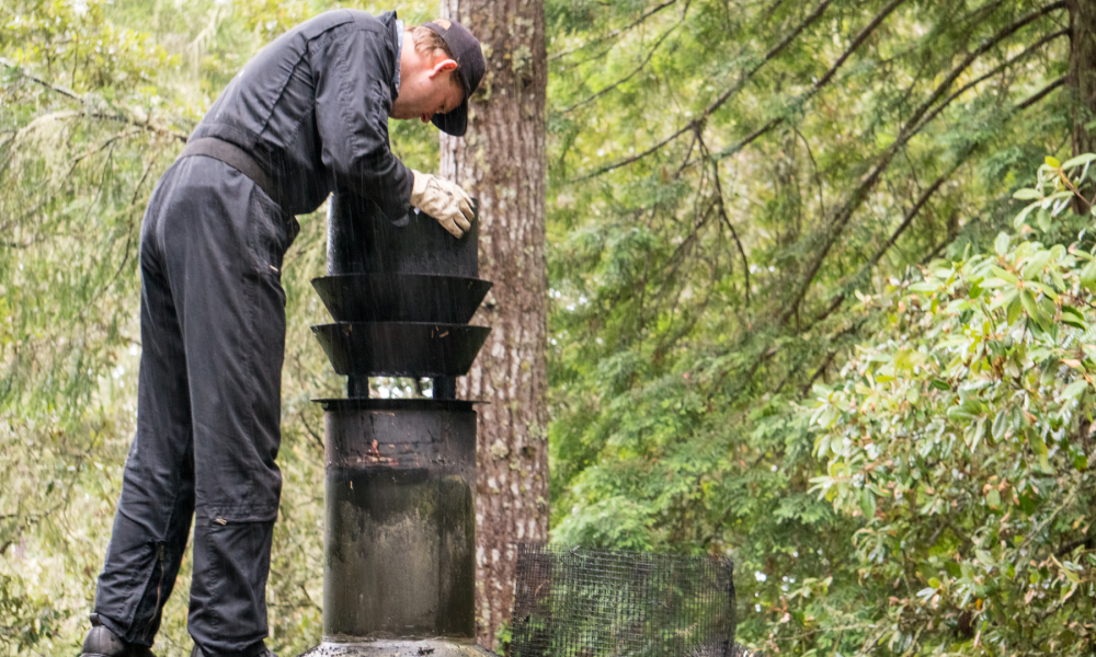 man looking down dirty chimney from roof