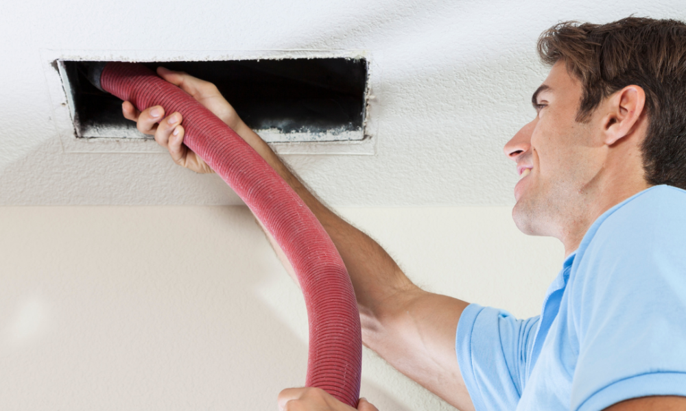 Service technician inserting air duct cleaning tool into ceiling vent